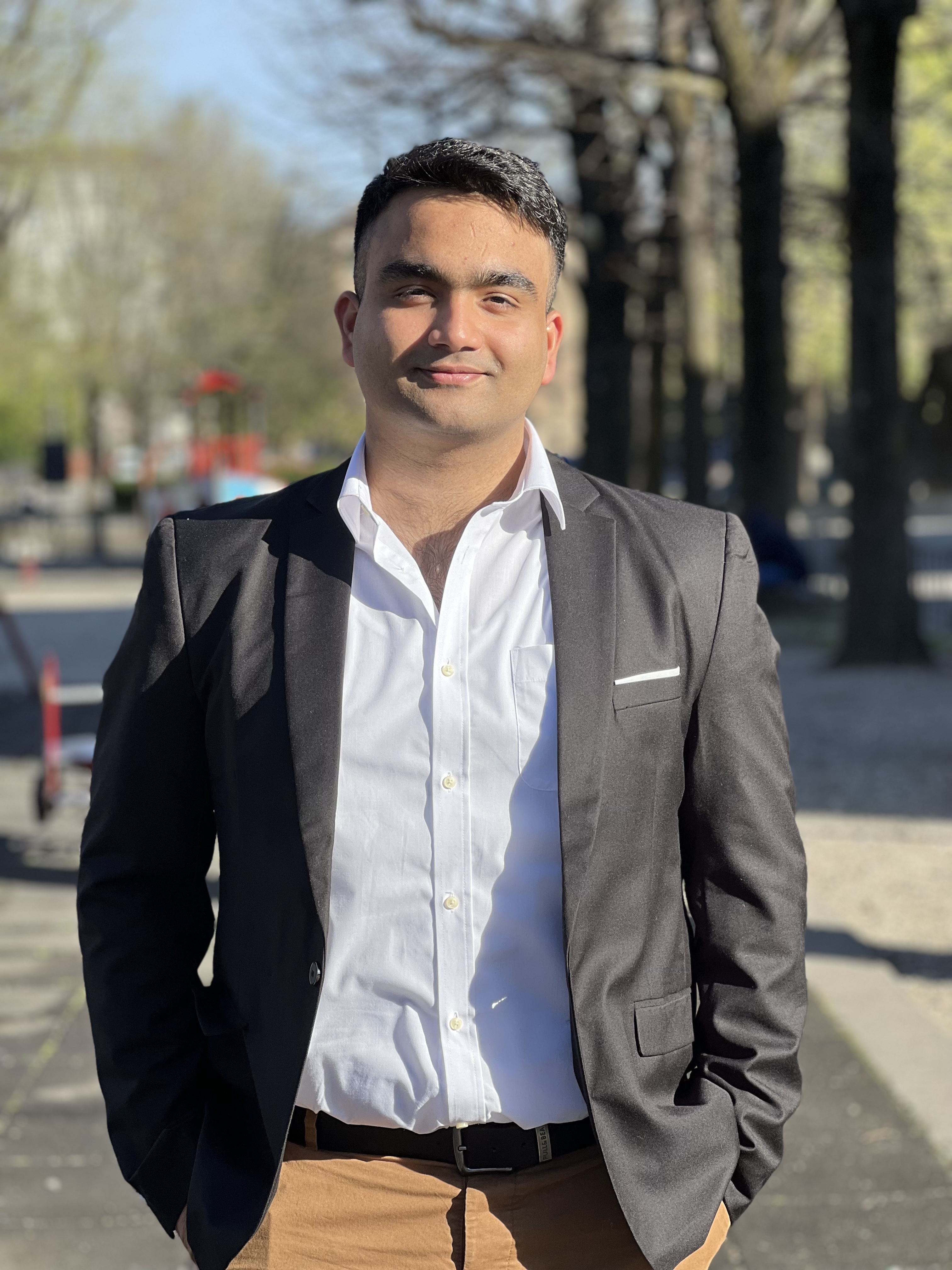 Muhammad Hamza Ali smiling in a black coat and white shirt